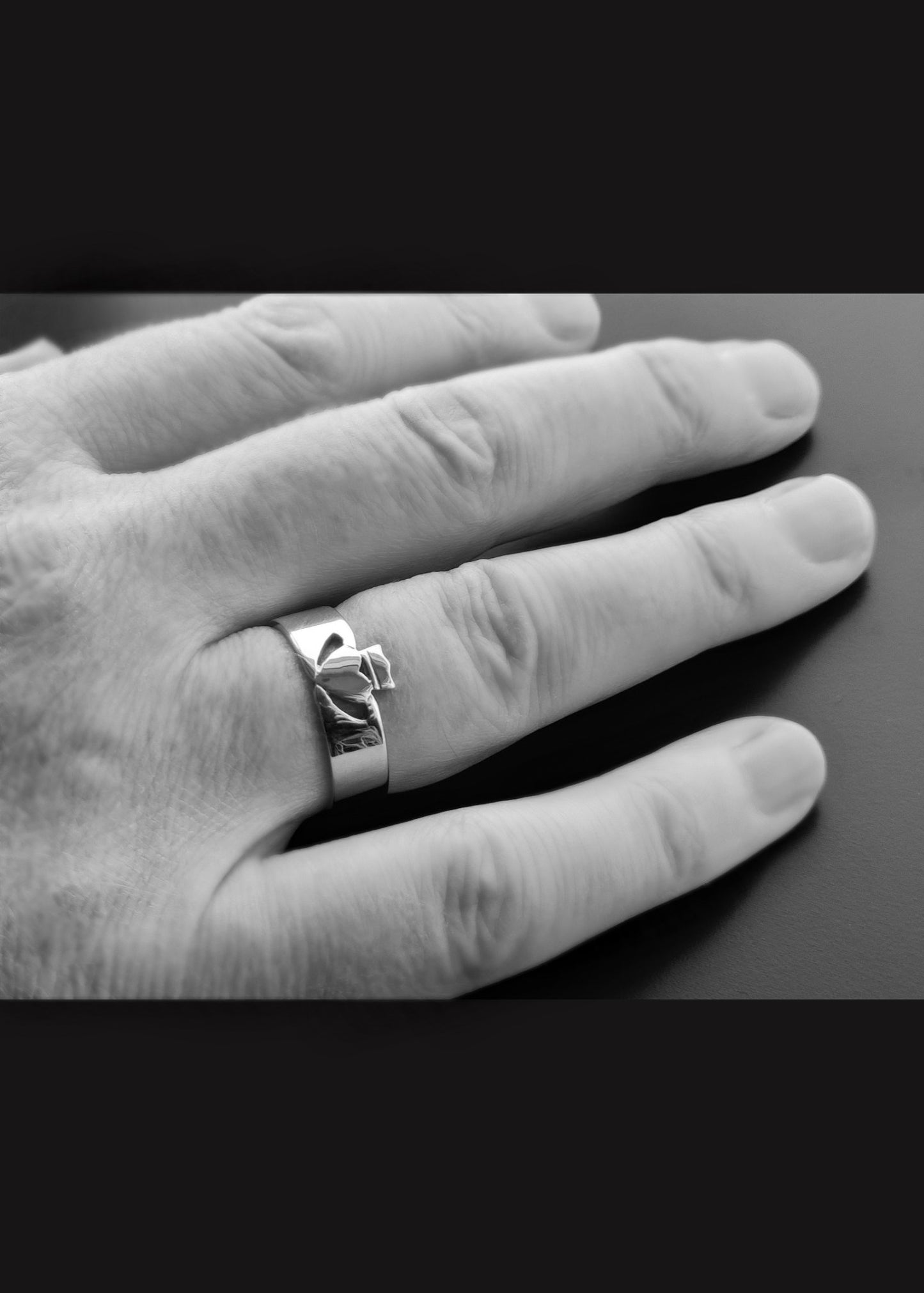This image shows the modern white gold men;'s claddagh ring in a polished finish o n a man's hand