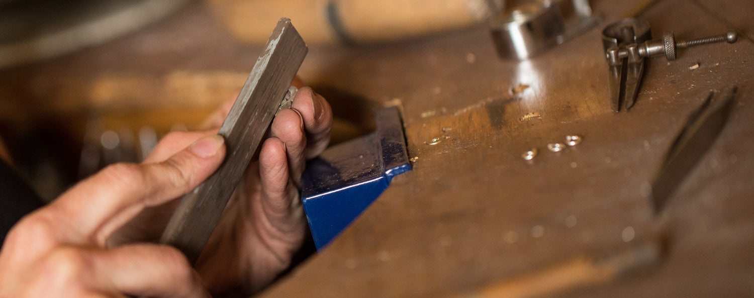 Filing a silver claddagh pendant on silversmith workshop bench