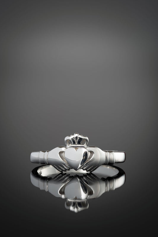 Silver claddagh ring on a reflective surface with a dark background